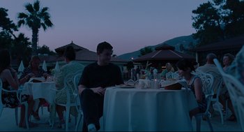 Movie still from “Aftersun” (2022), directed by Charlotte Wells – A group of people sitting at a table with food; Medium shot, Over the shoulder angle
