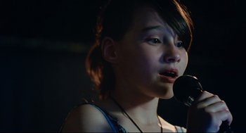 Movie still from “Aftersun” (2022), directed by Charlotte Wells – A young girl is singing into a microphone; Close Up shot, Over the shoulder angle