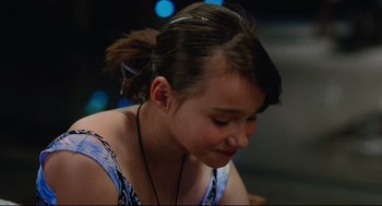Movie still from “Aftersun” (2022), directed by Charlotte Wells – A young woman with a ponytail sitting in front of some lights; Close Up shot, Over the shoulder angle
