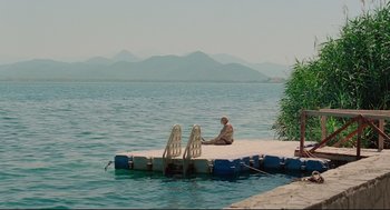Movie still from “Aftersun” (2022), directed by Charlotte Wells – A man sitting on a dock in the middle of a lake; Extreme Wide shot, High angle