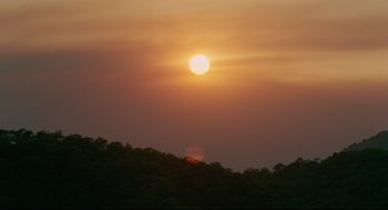 Movie still from “Aftersun” (2022), directed by Charlotte Wells – The sun is setting over a wooded area; Extreme Wide shot, Low angle