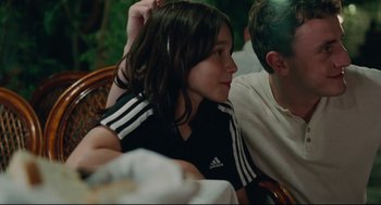 Movie still from “Aftersun” (2022), directed by Charlotte Wells – A young girl sitting next to an older man; Medium shot, Over the shoulder angle