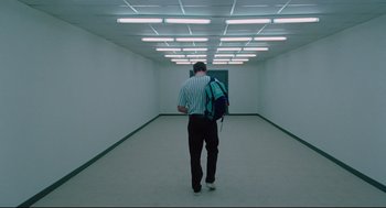Movie still from “Aftersun” (2022), directed by Charlotte Wells – A man walking down a hallway with a backpack; Wide shot, Low angle
