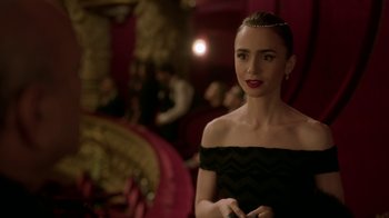 Movie still from “Emily in Paris” (2020), created by Darren Star – A woman in a black dress is posing for a picture; Medium shot, Over the shoulder angle