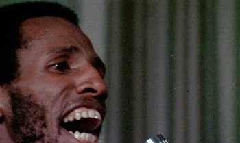 Movie still from “Ganja & Hess” (1973), directed by Bill Gunn – A person singing into a microphone; Extreme Close Up shot, Low angle