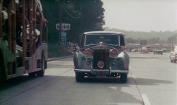 Movie still from “Ganja & Hess” (1973), directed by Bill Gunn – An old car driving down a street next to a double decker bus; Extreme Wide shot, High angle