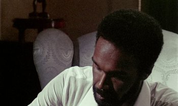 Movie still from “Ganja & Hess” (1973), directed by Bill Gunn – A man sitting in front of a chair looking down at the floor; Close Up shot, High angle