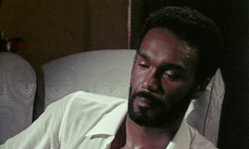 Movie still from “Ganja & Hess” (1973), directed by Bill Gunn – A man with a beard and a white shirt is laying on a couch; Close Up shot, High angle