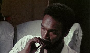 Movie still from “Ganja & Hess” (1973), directed by Bill Gunn – A man sitting in a chair with a cigarette in his mouth; Close Up shot, High angle