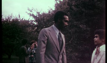 Movie still from “Ganja & Hess” (1973), directed by Bill Gunn – A man wearing a suit and tie walking in a park; Medium shot, Low angle