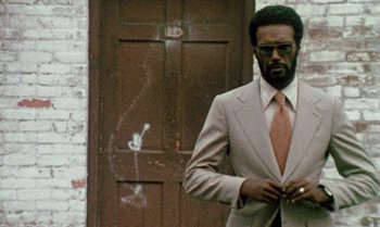 Movie still from “Ganja & Hess” (1973), directed by Bill Gunn – A man in a suit and tie standing in front of a door; Medium shot, Low angle