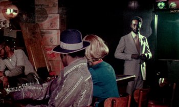 Movie still from “Ganja & Hess” (1973), directed by Bill Gunn – A man and a woman sitting at a table in front of another man; Medium shot, Over the shoulder angle