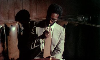 Movie still from “Ganja & Hess” (1973), directed by Bill Gunn – A man sitting at a table with a glass of beer; Medium shot, Low angle