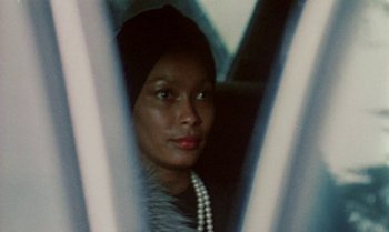 Movie still from “Ganja & Hess” (1973), directed by Bill Gunn – A woman wearing a pearl necklace looking out a window; Close Up shot, Over the shoulder angle