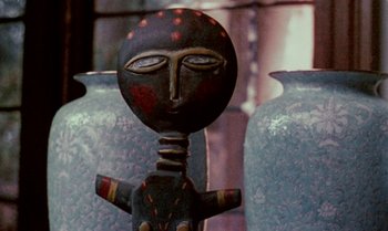 Movie still from “Ganja & Hess” (1973), directed by Bill Gunn – A black and red statue sitting in front of two blue vases; Extreme Close Up shot, Low angle