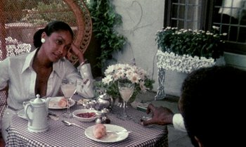 Movie still from “Ganja & Hess” (1973), directed by Bill Gunn – A woman sitting at a table with a plate of food; Medium shot, High angle
