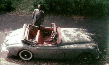 Movie still from “Ganja & Hess” (1973), directed by Bill Gunn – A man standing next to an old fashioned car; Wide shot, High angle