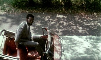 Movie still from “Ganja & Hess” (1973), directed by Bill Gunn – A man sitting on the back of a red motorcycle; Wide shot, High angle