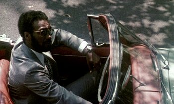 Movie still from “Ganja & Hess” (1973), directed by Bill Gunn – A man in a suit driving a vintage car; Medium shot, High angle