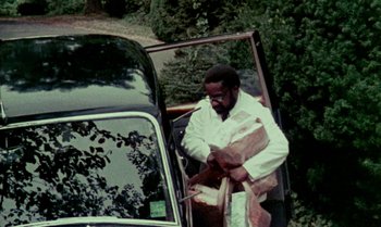 Movie still from “Ganja & Hess” (1973), directed by Bill Gunn – A man loading groceries into the back of a car; Medium shot, High angle