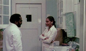 Movie still from “Ganja & Hess” (1973), directed by Bill Gunn – A man and a woman standing next to each other in a kitchen; Medium shot, Over the shoulder angle