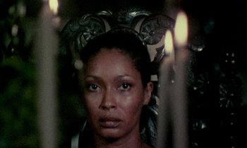 Movie still from “Ganja & Hess” (1973), directed by Bill Gunn – A woman is standing in front of some candles; Close Up shot, Over the shoulder angle