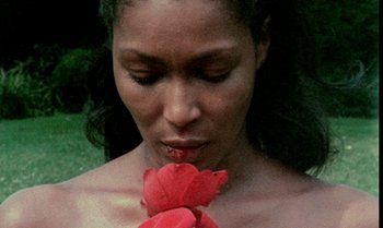 Movie still from “Ganja & Hess” (1973), directed by Bill Gunn – A woman is holding a red flower in her mouth; Close Up shot, High angle