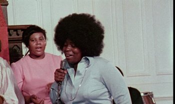 Movie still from “Ganja & Hess” (1973), directed by Bill Gunn – A woman with a large afro singing into a microphone; Medium shot, Low angle