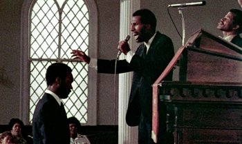 Movie still from “Ganja & Hess” (1973), directed by Bill Gunn – A man in a suit is singing into a microphone; Medium shot, Low angle