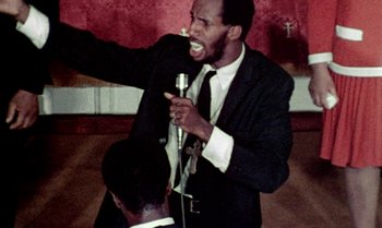 Movie still from “Ganja & Hess” (1973), directed by Bill Gunn – A man in a suit and tie holding a microphone; Close Up shot, Low angle