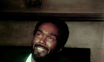 Movie still from “Ganja & Hess” (1973), directed by Bill Gunn – A person with a beard smiling; Close Up shot, Over the shoulder angle