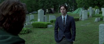 Movie still from “Garden State” (2004), directed by Zach Braff – A man in a suit standing in front of a grave yard; Medium shot, Low angle