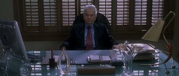 Movie still from “Garden State” (2004), directed by Zach Braff – An older man sitting at a desk in a suit and tie; Medium shot, Low angle