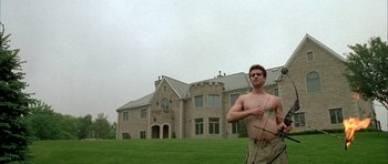 Movie still from “Garden State” (2004), directed by Zach Braff – A man holding a bow and arrow in front of a large house; Wide shot, Low angle