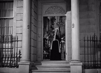 Movie still from “Gaslight” (1944), directed by George Cukor – A black and white photo of a woman sitting on a chair in front of a door; Wide shot, Low angle