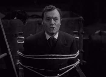 Movie still from “Gaslight” (1944), directed by George Cukor – A black and white photo of a man tied to a chair; Medium shot, High angle