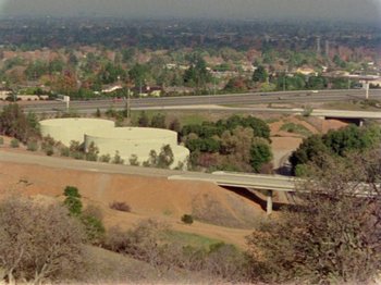 Movie still from “Gates of Heaven” (1978), directed by Errol Morris – An aerial view of a freeway and a city in the distance; Extreme Wide shot, High angle