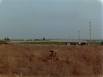 Movie still from “Gates of Heaven” (1978), directed by Errol Morris – An empty field with a highway in the background; Extreme Wide shot, Low angle