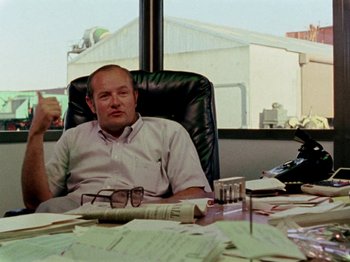 Movie still from “Gates of Heaven” (1978), directed by Errol Morris – A man sitting at a table with papers on the table; Medium shot, Low angle