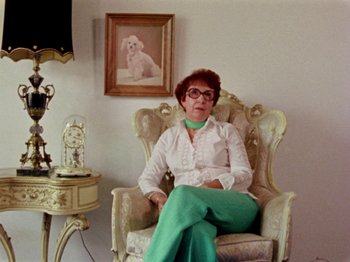 Movie still from “Gates of Heaven” (1978), directed by Errol Morris – An older woman sitting in a chair in a room; Medium shot, Low angle