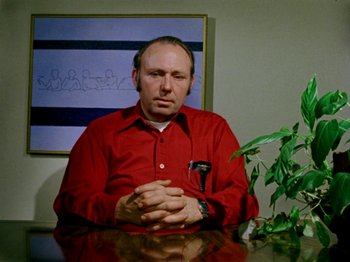 Movie still from “Gates of Heaven” (1978), directed by Errol Morris – A man sitting at a table in front of a painting; Medium shot, Low angle