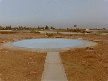 Movie still from “Gates of Heaven” (1978), directed by Errol Morris – An empty concrete circle in the middle of an empty field; Extreme Wide shot, High angle