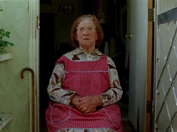 Movie still from “Gates of Heaven” (1978), directed by Errol Morris – An older woman wearing a red apron and glasses; Medium shot, High angle