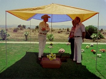 Movie still from “Gates of Heaven” (1978), directed by Errol Morris – A group of men standing under an umbrella; Wide shot, High angle