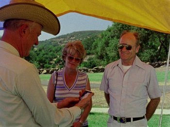 Movie still from “Gates of Heaven” (1978), directed by Errol Morris – A group of people standing under an umbrella; Medium shot, High angle