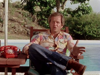 Movie still from “Gates of Heaven” (1978), directed by Errol Morris – A man sitting in a chair near a body of water; Medium shot, High angle