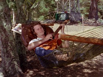 Movie still from “Gates of Heaven” (1978), directed by Errol Morris – A woman sitting in a hammock playing a guitar; Wide shot, High angle