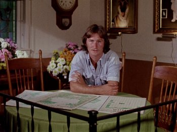 Movie still from “Gates of Heaven” (1978), directed by Errol Morris – A man sitting at a table in front of a clock; Medium shot, High angle
