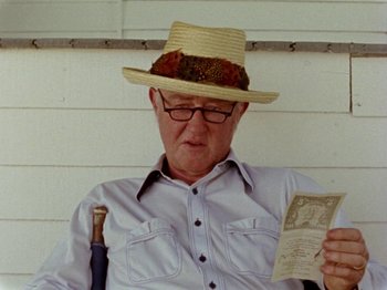 Movie still from “Gates of Heaven” (1978), directed by Errol Morris – An older man wearing a straw hat and holding an umbrella; Close Up shot, Low angle