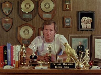 Movie still from “Gates of Heaven” (1978), directed by Errol Morris – A man sitting at a table with many trophies on top of it; Medium shot, Low angle